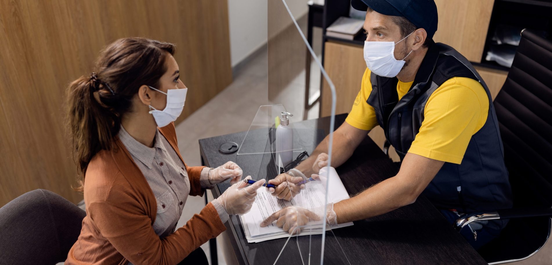 Manager of auto repair shop giving to customer a paperwork to sign while wearing protective face masks in the office.